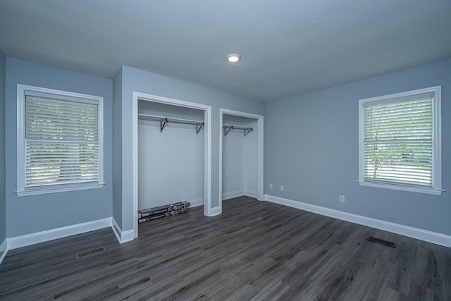 unfurnished bedroom featuring dark wood-style flooring, two closets, baseboards, and recessed lighting