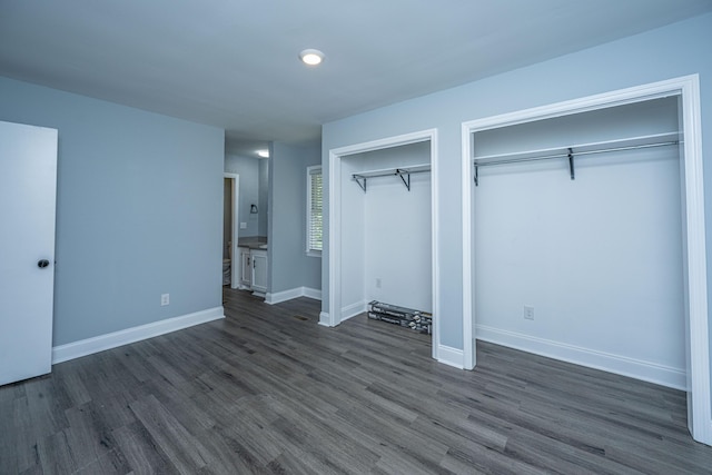 unfurnished bedroom with two closets, dark wood-style floors, baseboards, and recessed lighting