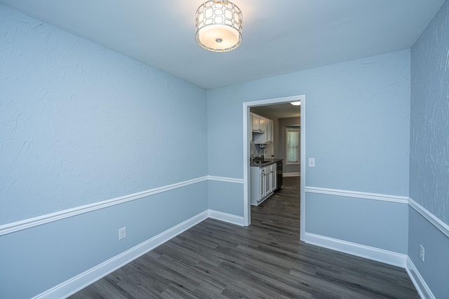 unfurnished room with dark wood finished floors, baseboards, and a sink