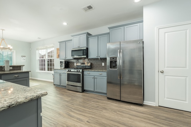 kitchen with appliances with stainless steel finishes, pendant lighting, decorative backsplash, light stone countertops, and light wood-type flooring