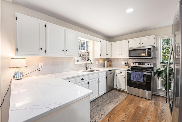 kitchen with light wood finished floors, tasteful backsplash, appliances with stainless steel finishes, white cabinets, and a sink