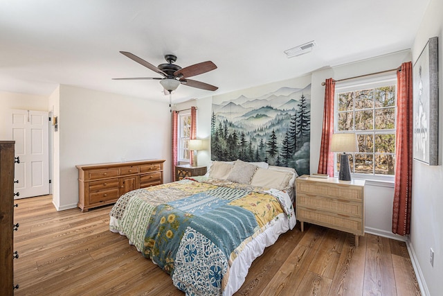 bedroom with a ceiling fan, hardwood / wood-style flooring, visible vents, and baseboards