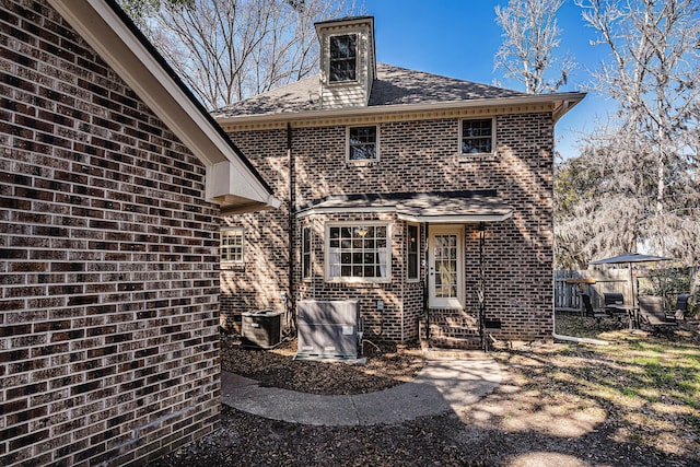 back of house with a shingled roof, entry steps, brick siding, and fence