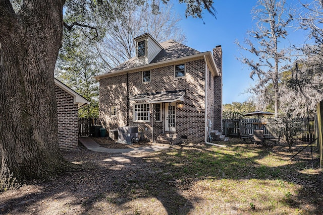 back of house with brick siding, fence, a chimney, and a lawn