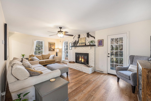 living area with hardwood / wood-style floors, a fireplace, a ceiling fan, and baseboards