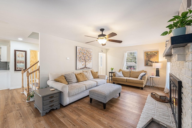 living room with stairs, a stone fireplace, wood finished floors, and a ceiling fan