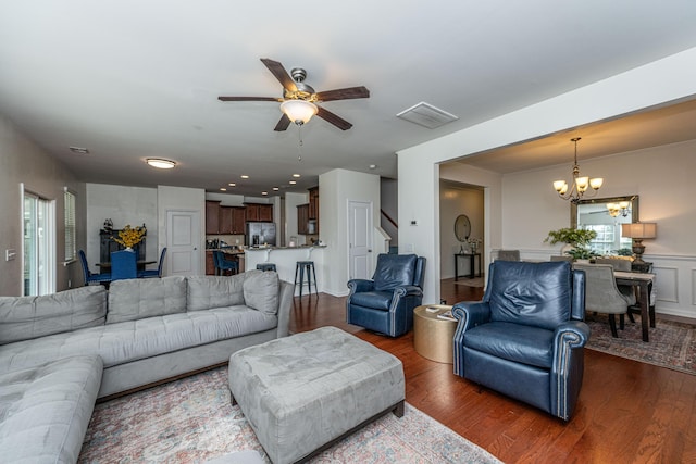 living area with visible vents, wood finished floors, stairway, a wainscoted wall, and ceiling fan with notable chandelier