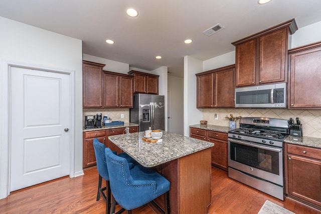 kitchen featuring stainless steel appliances, visible vents, light stone counters, and light wood finished floors