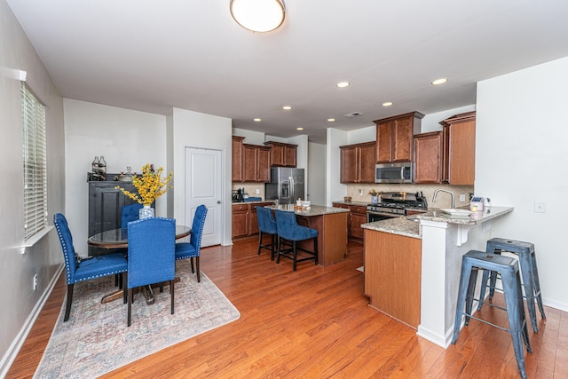 kitchen featuring backsplash, a kitchen bar, appliances with stainless steel finishes, light stone counters, and light wood finished floors