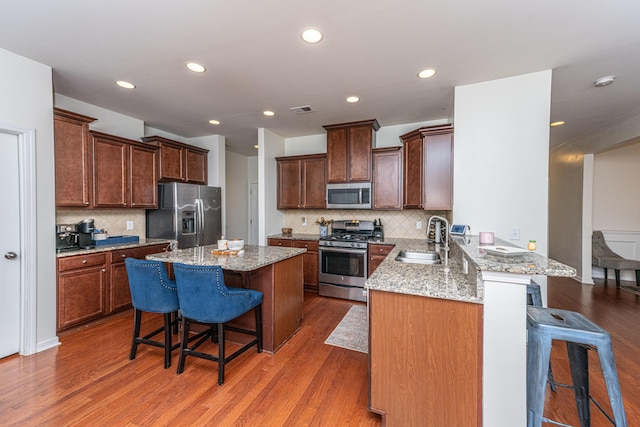 kitchen featuring a sink, appliances with stainless steel finishes, wood finished floors, and a breakfast bar area
