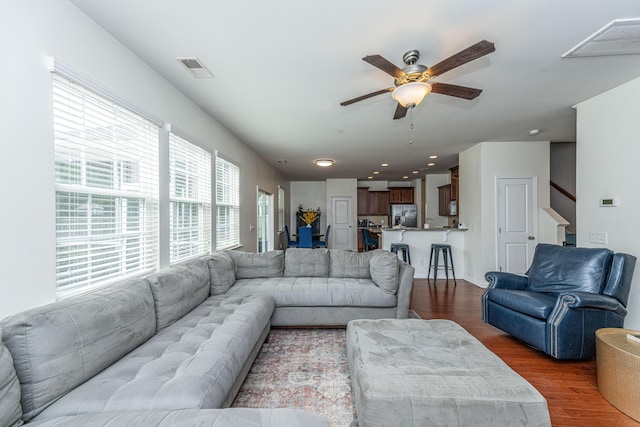 living area featuring dark wood-type flooring, ceiling fan, visible vents, and stairway