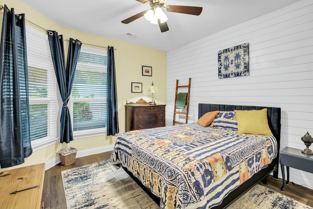 bedroom with dark hardwood / wood-style flooring, ceiling fan, and wooden walls