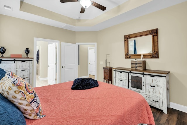 bedroom with ceiling fan, dark hardwood / wood-style floors, a raised ceiling, and ensuite bath