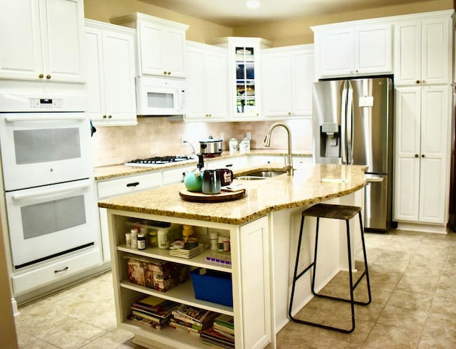 kitchen featuring light stone counters, white appliances, sink, a center island with sink, and white cabinets