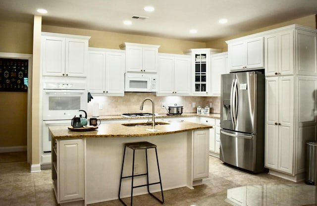 kitchen with tasteful backsplash, white appliances, sink, white cabinetry, and an island with sink