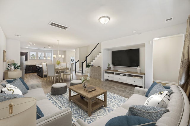 living area featuring an inviting chandelier, stairs, visible vents, and wood finished floors