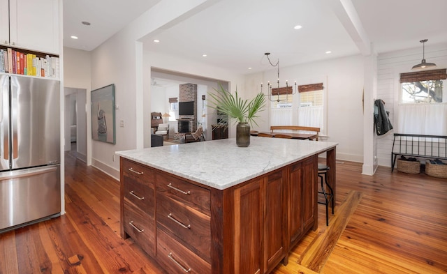 kitchen with a kitchen island, hanging light fixtures, stainless steel fridge, a notable chandelier, and hardwood / wood-style flooring