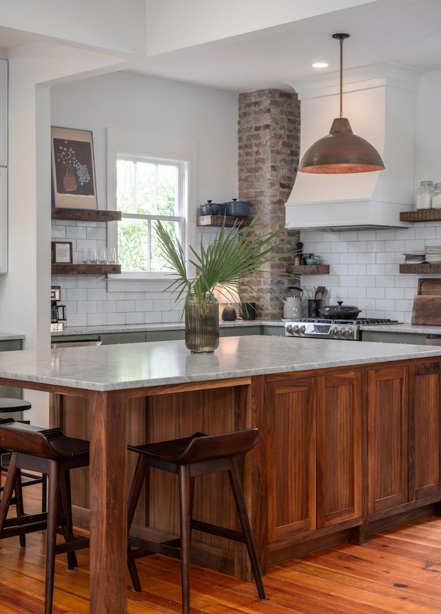 kitchen with tasteful backsplash, decorative light fixtures, a breakfast bar, light wood-type flooring, and light stone countertops