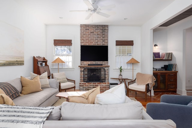 living room featuring ceiling fan, wood-type flooring, and a brick fireplace