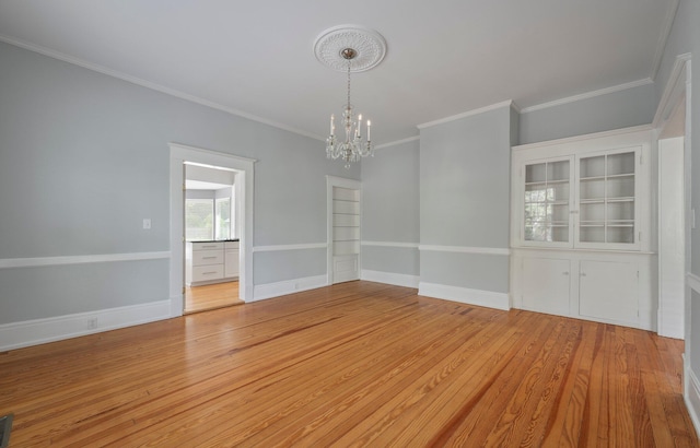 spare room with a chandelier, ornamental molding, and light wood-type flooring