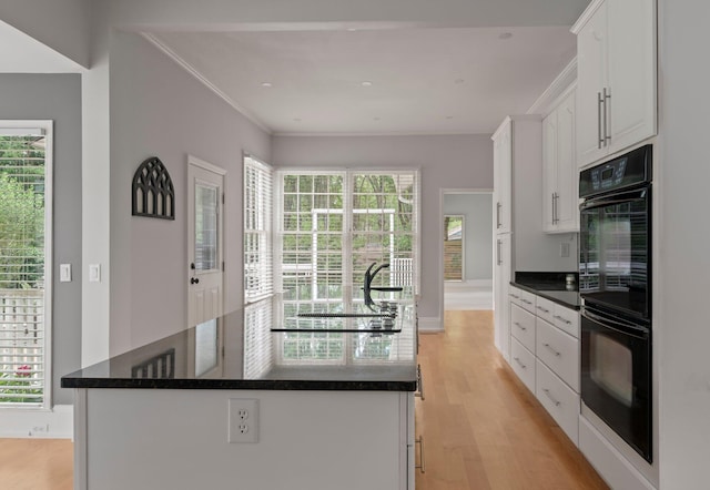 kitchen featuring light hardwood / wood-style floors, an island with sink, dark stone countertops, white cabinets, and double oven