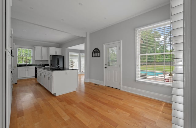 kitchen with black fridge, white cabinetry, a kitchen island, light hardwood / wood-style flooring, and sink