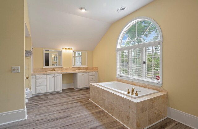 bathroom with vaulted ceiling, hardwood / wood-style floors, a relaxing tiled bath, vanity, and toilet