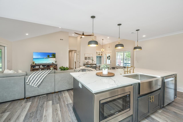 kitchen with light stone countertops, a center island with sink, decorative light fixtures, light wood-type flooring, and lofted ceiling