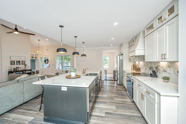 kitchen with white cabinetry, premium range hood, light hardwood / wood-style floors, and a center island with sink