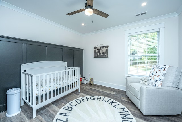 bedroom featuring dark hardwood / wood-style flooring, a crib, ceiling fan, and crown molding