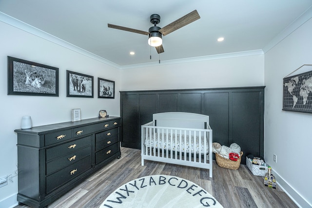 bedroom featuring hardwood / wood-style floors, a crib, ceiling fan, and crown molding