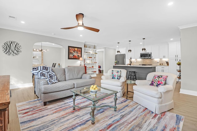 living room with ornamental molding, ceiling fan with notable chandelier, and light wood-type flooring