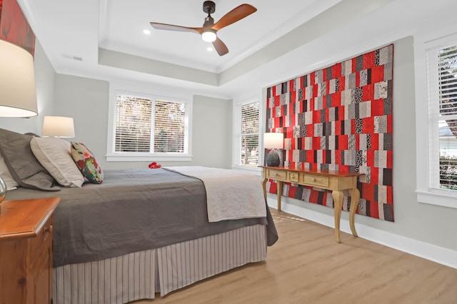 bedroom featuring multiple windows, hardwood / wood-style floors, a raised ceiling, and ceiling fan