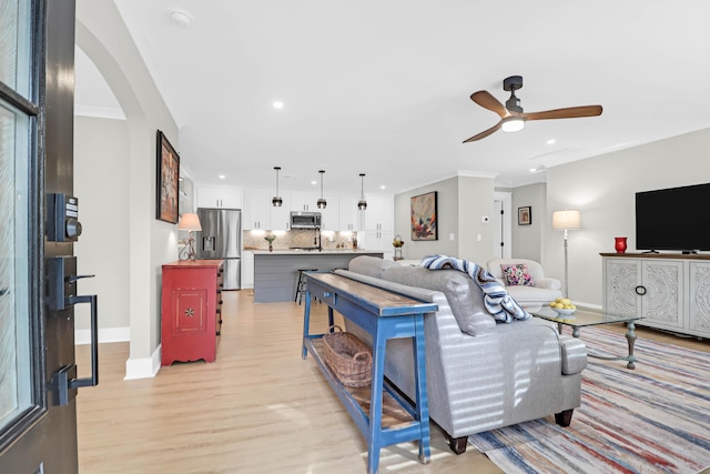 living room featuring light wood-type flooring, ceiling fan, and crown molding