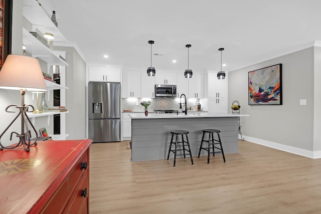 kitchen featuring backsplash, a center island with sink, appliances with stainless steel finishes, light hardwood / wood-style floors, and white cabinetry