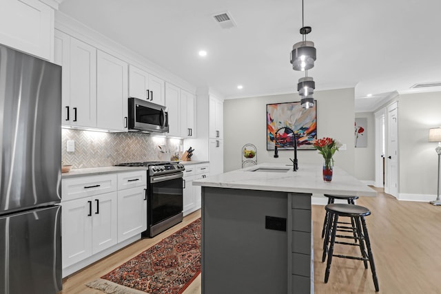 kitchen with stainless steel appliances, white cabinetry, and an island with sink