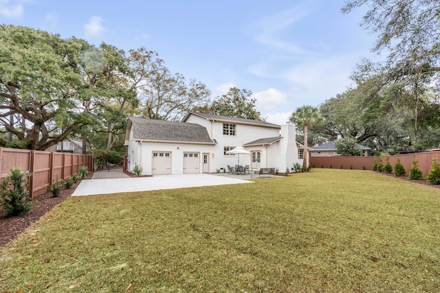 rear view of property featuring a lawn, a garage, and a patio