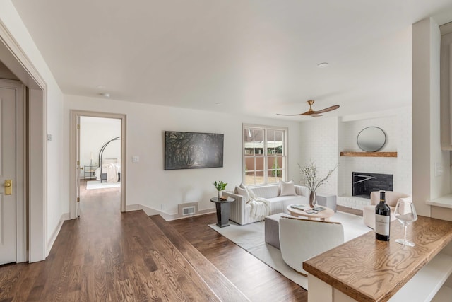 living room with dark hardwood / wood-style floors, ceiling fan, and a fireplace