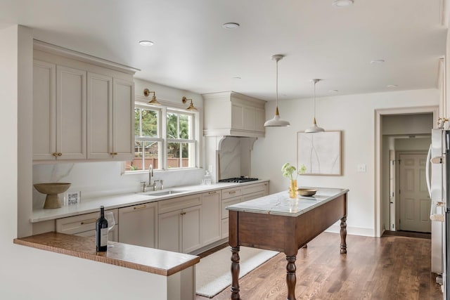 kitchen featuring gas cooktop, sink, wood-type flooring, decorative light fixtures, and a center island