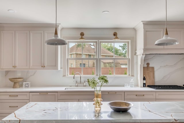 kitchen featuring sink, hanging light fixtures, stainless steel gas cooktop, light stone counters, and backsplash