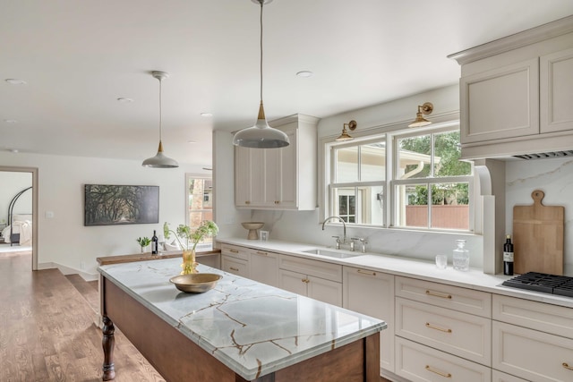 kitchen featuring sink, stainless steel gas cooktop, backsplash, pendant lighting, and light wood-type flooring