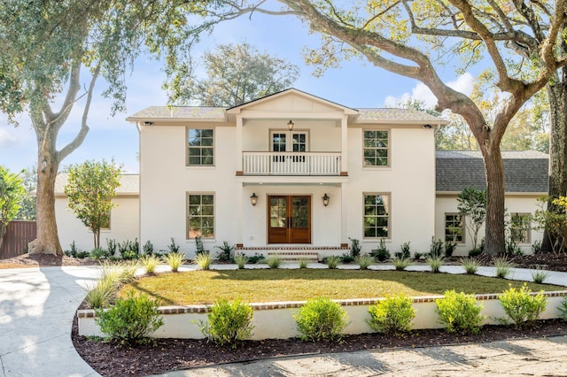 view of front facade featuring a balcony, a front yard, and french doors