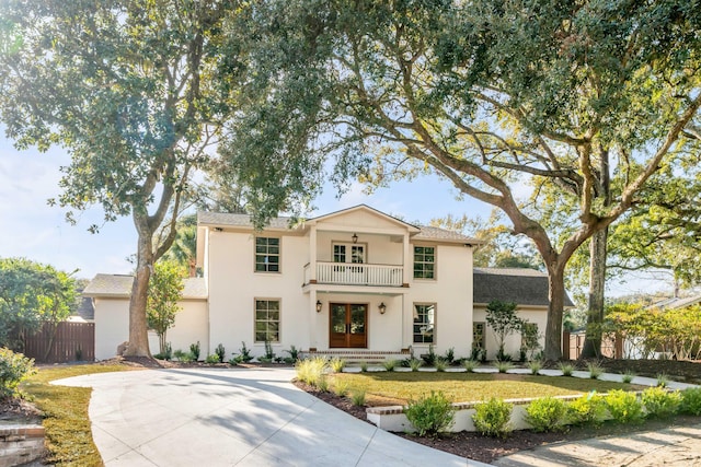 view of front facade featuring a balcony, a front yard, and french doors