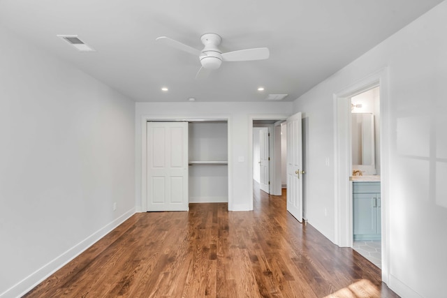 unfurnished bedroom featuring ensuite bathroom, ceiling fan, dark wood-type flooring, and a closet