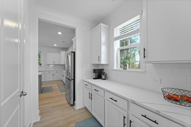 kitchen with freestanding refrigerator, white cabinets, backsplash, light wood-type flooring, and light stone counters