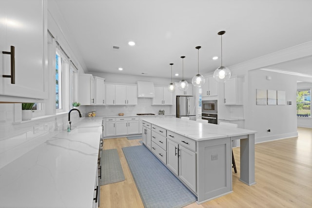 kitchen with appliances with stainless steel finishes, wall chimney exhaust hood, ornamental molding, a kitchen bar, and white cabinetry