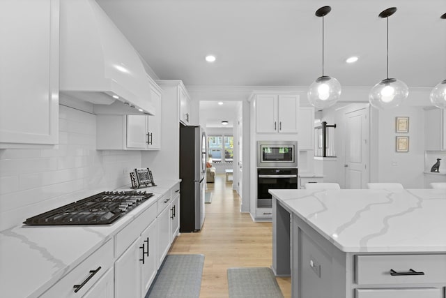 kitchen featuring stainless steel appliances, premium range hood, light wood-style flooring, white cabinetry, and decorative backsplash