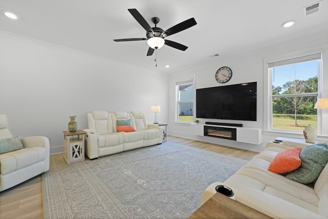living room with wood finished floors, recessed lighting, ornamental molding, a ceiling fan, and a glass covered fireplace