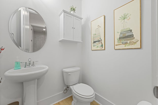 half bathroom featuring baseboards, wood finished floors, toilet, and a sink
