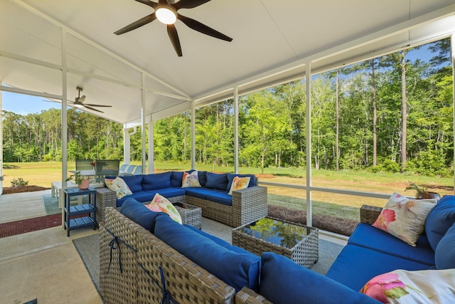 sunroom with a ceiling fan, outdoor lounge area, lofted ceiling, and view of wooded area